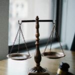 Decorative judgement scale and gavel placed on desk in light lawyer office against window